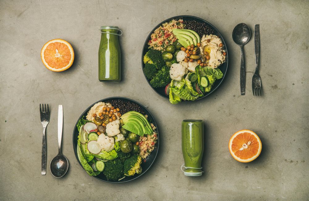 Two vegetarian bowls, with smoothie, orange halves, silverware