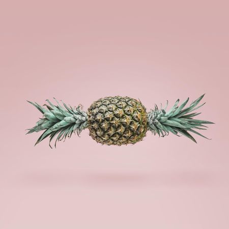 Pineapple in shape of candy with green top on both ends on blush background