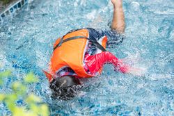 Child in life jacket with head down in water