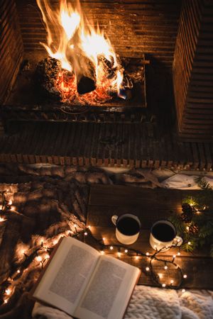 Unrecognizable woman sitting by fireplace and reading book