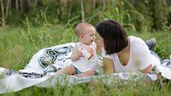 Pleasant mother and baby lying on blanket on picnic in field
