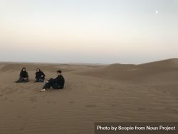 Two women wearing hijab and a man sitting on sand in desert 0Jyjvb