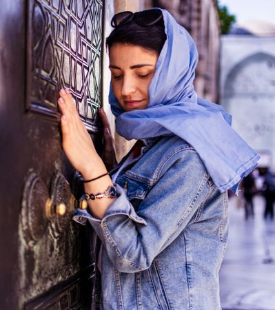 Woman in blue veil and denim jacket standing in front of wood carved wall