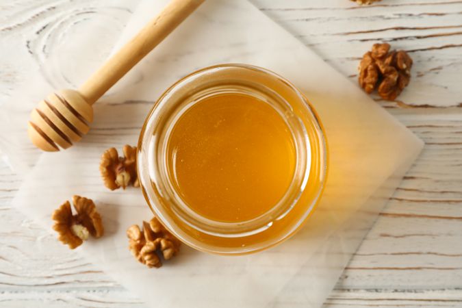 Walnuts, dipper, parchment and glass jar with honey on neutral background, top view