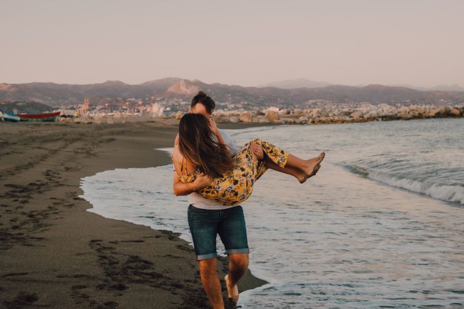 Amorous man carrying woman on arms along sandy beach