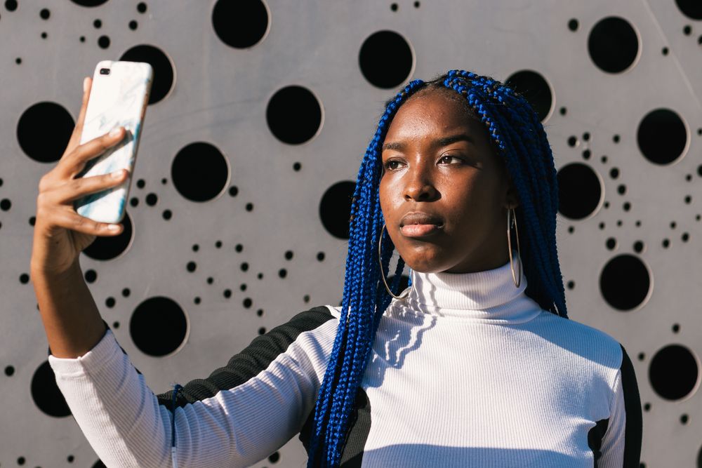 Serious Black woman taking selfie on street