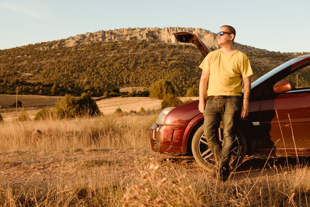Man leaning in broken car in countryside