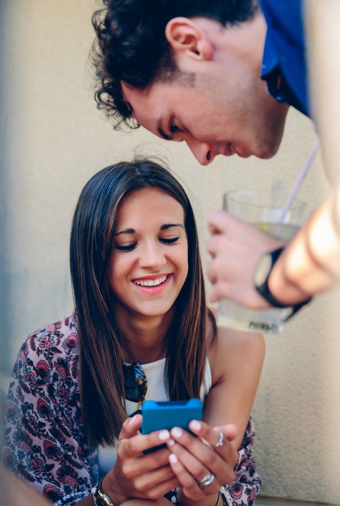 Smiling woman looking a smartphone with her friend outdoors