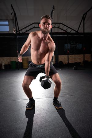 Strong sportsman doing exercises with dumbbell in gym