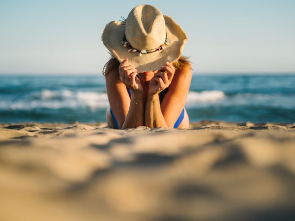 Sandy beach and woman in hat tanning