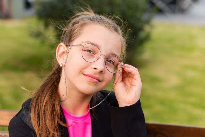 Girl adjusting glasses while sitting on park bench