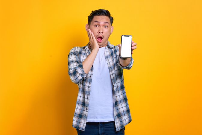 Surprised Asian male holding up smart phone with blank screen