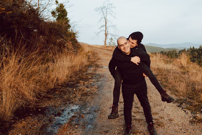 Smiling man holding on back cheerful guy on road on hill