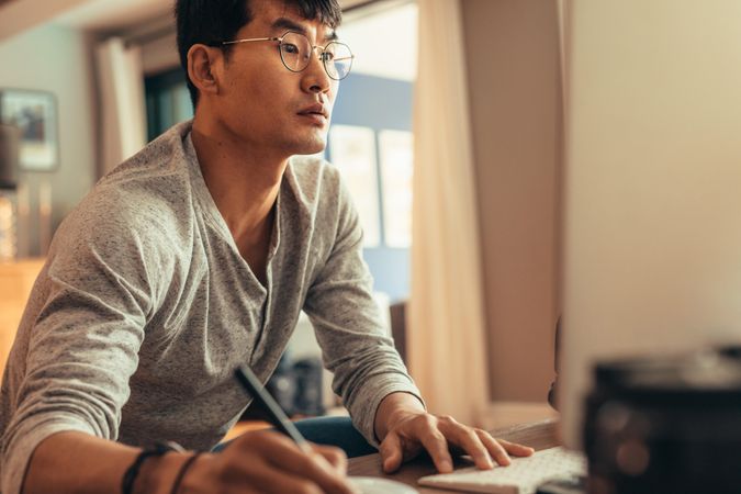 Asian man looking at computer screen and writing