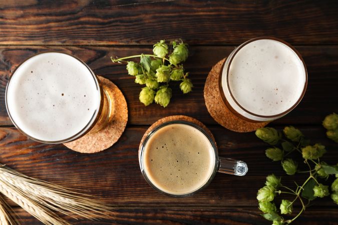 Mugs with beer and hop cones on wooden table, top view