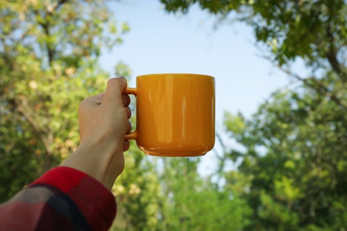 Female hand in shirt hold yellow cup outdoor