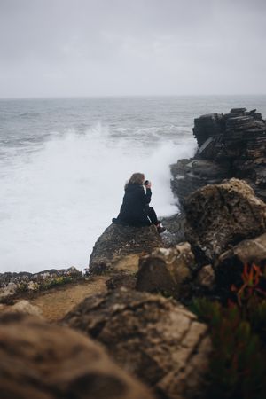 Woman sitting on coastal rocks with coffee