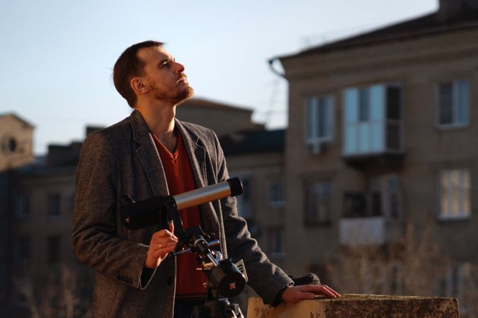 Astronomer rests beside telescope, analyzing sun on urban rooftop