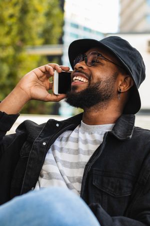 Trendy Black man talking smartphone on bench