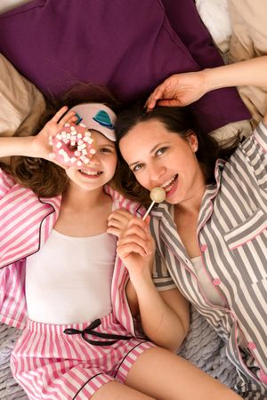Mother and daughter sharing joyful moment with donuts on bed.
