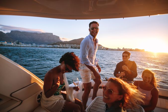 Smiling male standing on back of yacht while friends laugh