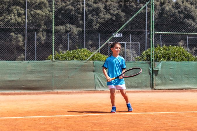 Little boy playing tennis on a dirt court