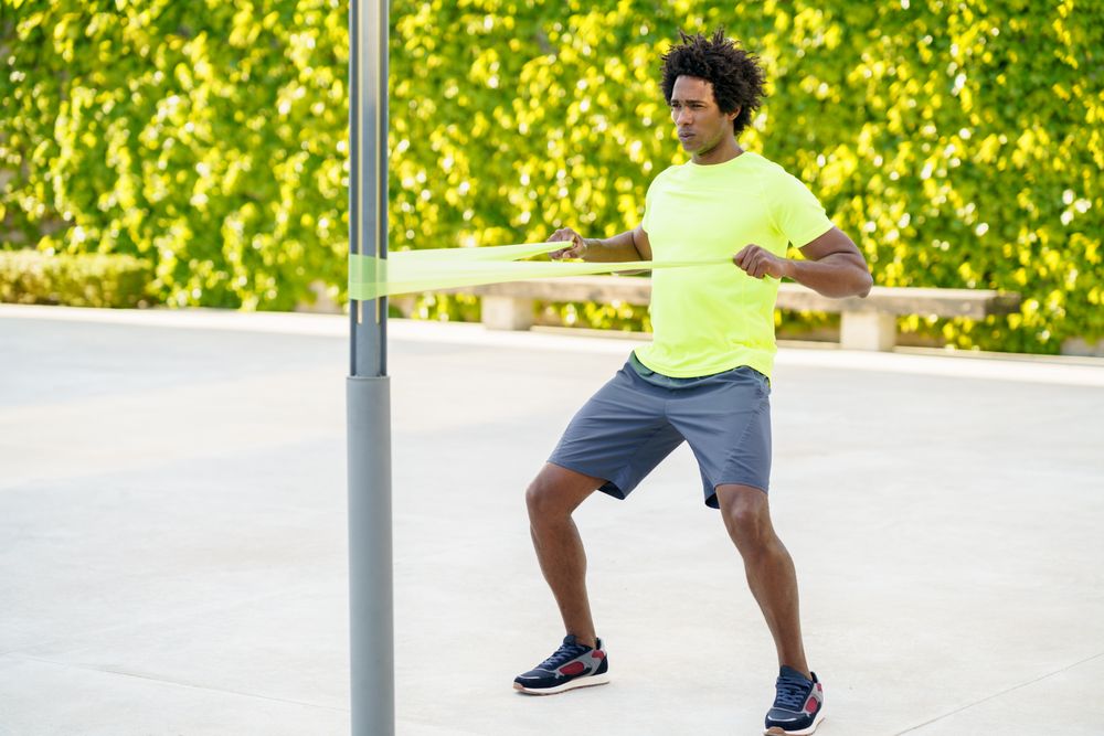 Man pulling back on resistance bands in front of hedge