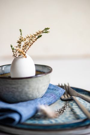 Side view of Easter table setting with decorative egg shell and heather on blue plates
