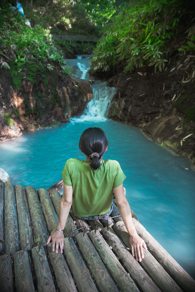 Back view of woman in green t-shirt sitting on wooden dock over blue river
