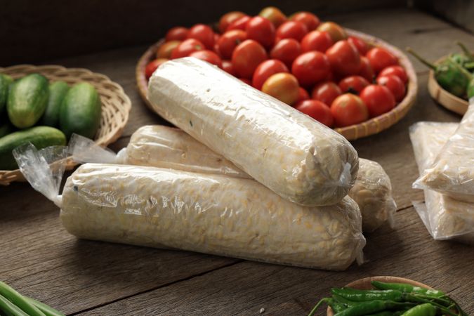 Cylinder Shape Raw Tempeh or Tempe with Plastic Wrapping beside Various Fresh Vegetable