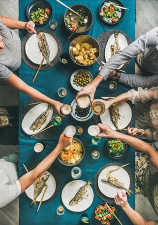 Group of people toasting drinks at table with whole fish on each plate and vegetable side dishes