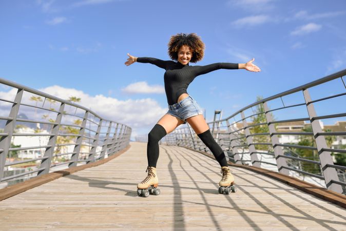 Woman with afro hairstyle in roller skates on wooden bridge with arms opened wide