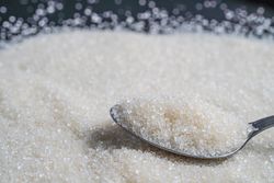 Granulated sugar spread on a surface with a spoonful resting on top