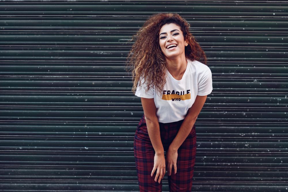 Happy Arab woman with curly hair leaning forward outside of metal security doors