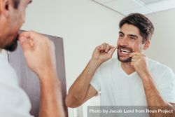 Man looking in the bathroom mirror and using dental floss to clean his teeth 43lgOb