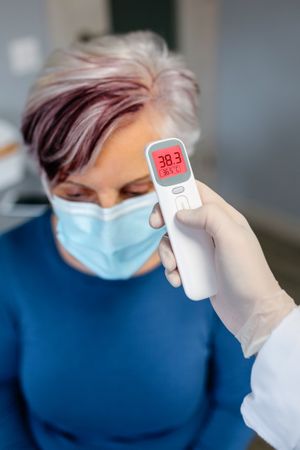 Mature woman with dyed hair has a fever whose temperature is taken by her doctor