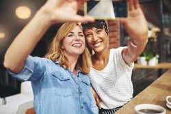 Two female friends sitting at a cafe table smiling and taking a selfie