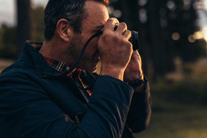 Close up of man looking through his camera to take photo standing outdoors