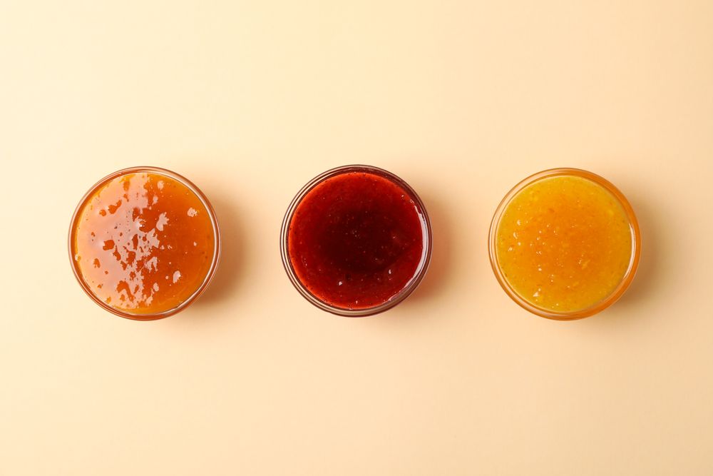 Bowls with jam on beige background, top view