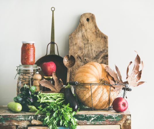 Fresh autumnal produce on kitchen counter, with squash, wooden board, apple, relish