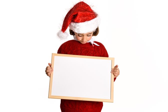 Child in Santa outfit holding blank board