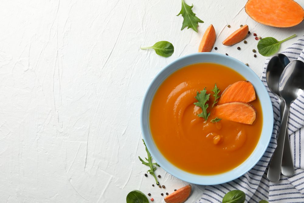 Sweet potato soup on table with salt pepper and spoons with copy space