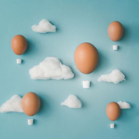 Hot air balloons made of decorated brown eggs with cotton clouds on bright blue background