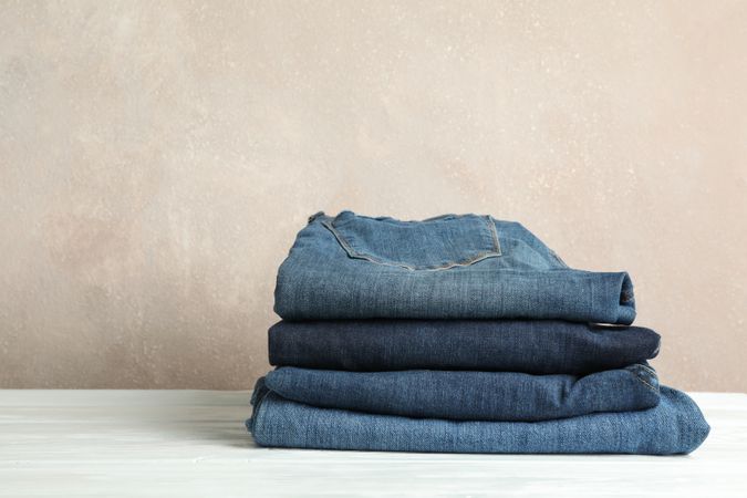 Stack of jeans pants on light background, space for text