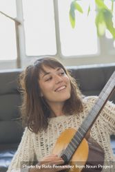 Happy female in wooly sweater looking at fretboard of guitar bGaKl5