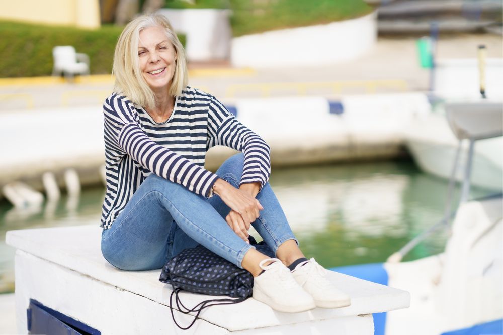 Happy older female relaxing on dock on sunny day