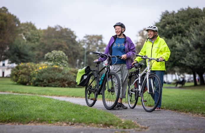 Two older people standing and talking with bikes looking away