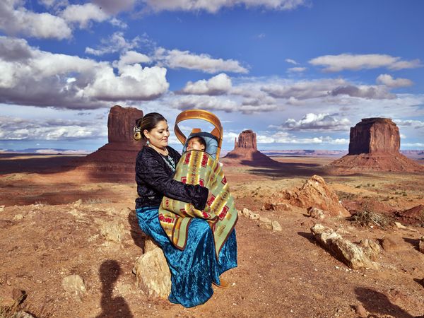 Navajo mother looking proudly at her baby atop mesa in Monument Valley