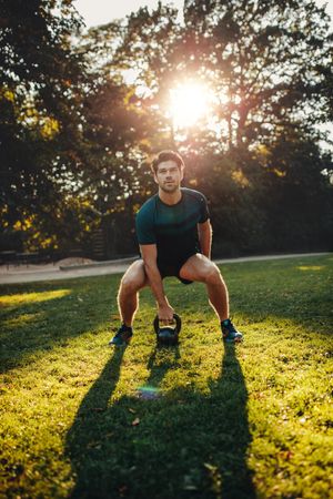 Vertical shot of strong young man exercising with kettle bell weights in the park