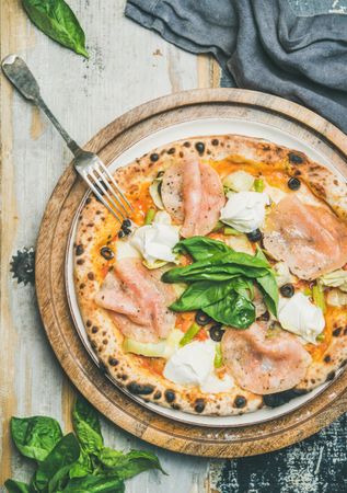 Freshly made wood fire oven pizza with spinach, ham and olives, close up, vertical composition